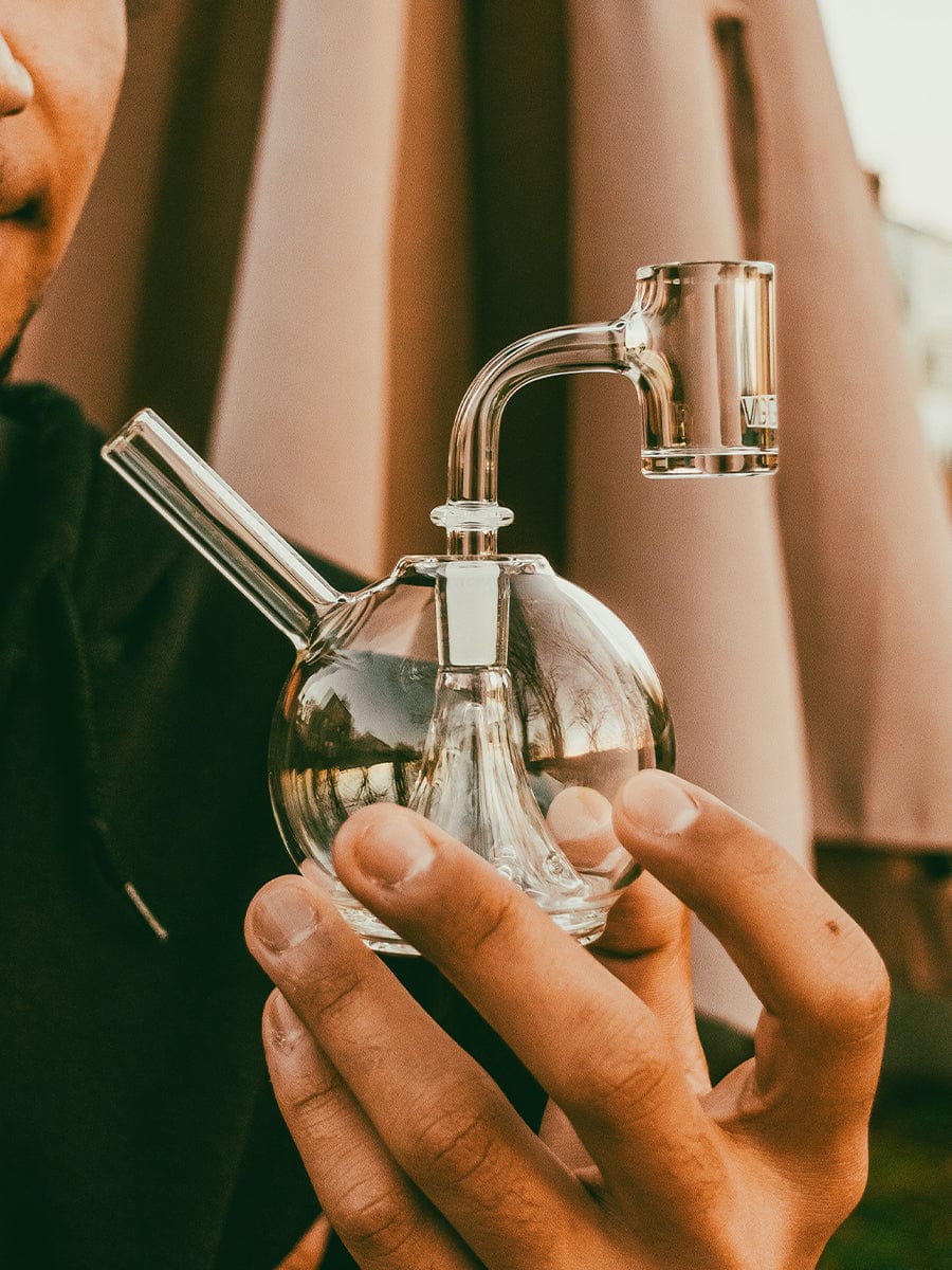 A hand holds the Eclipse Rig, showcasing the clear glass form against a blurred background.