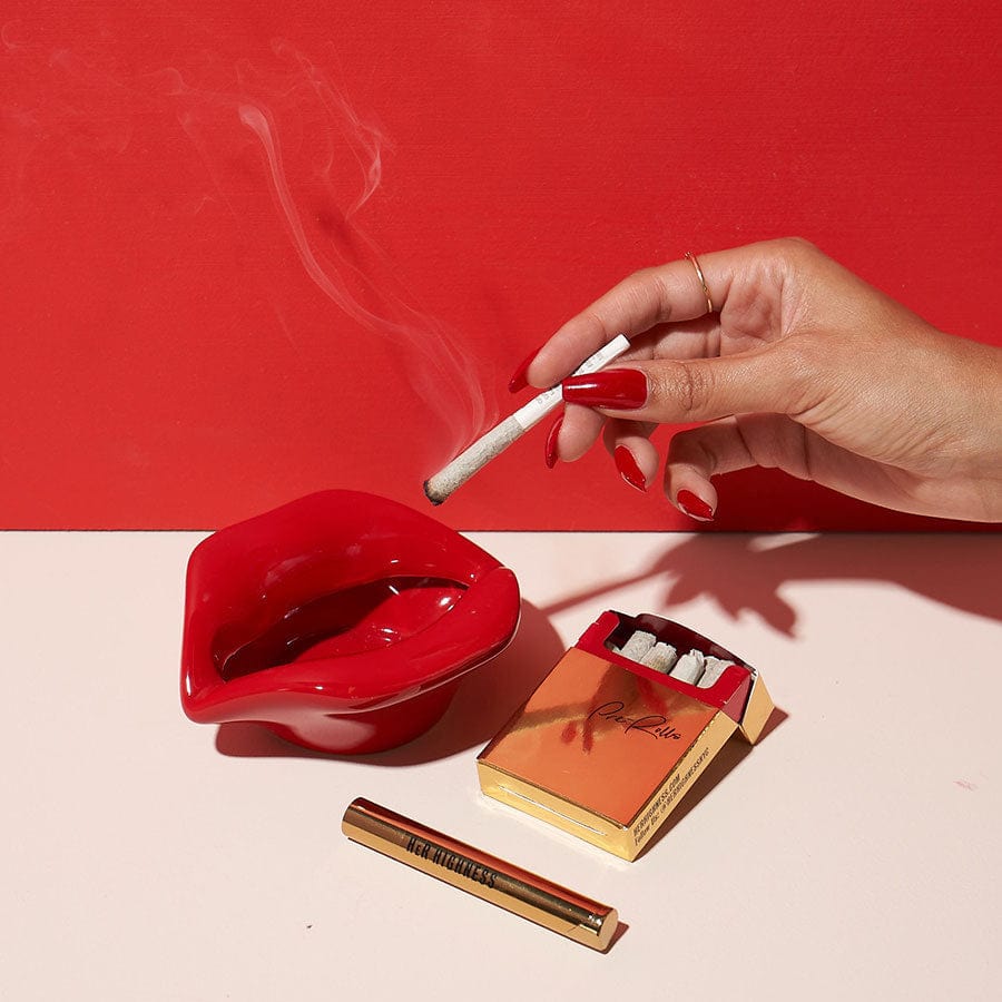 A close-up, high-angle shot shows a lit joint resting inside the red Lip Service Ashtray, highlighting its uniquely shaped design.