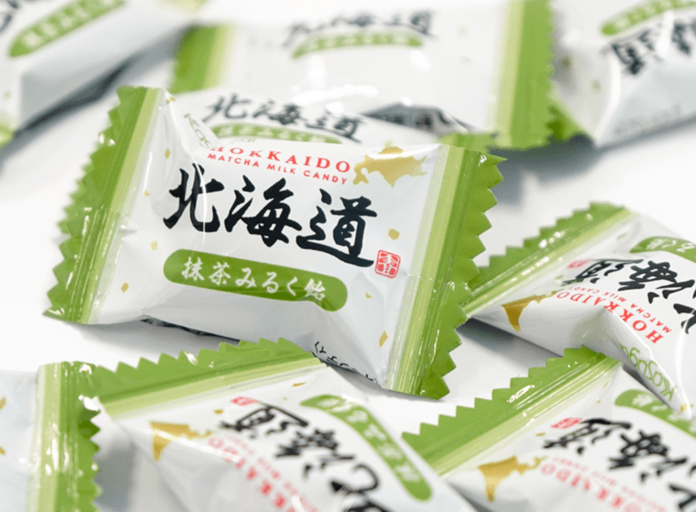 A close-up, angled view of Hokkaido Japanese Matcha Milk Candy individually wrapped in translucent green cellophane.