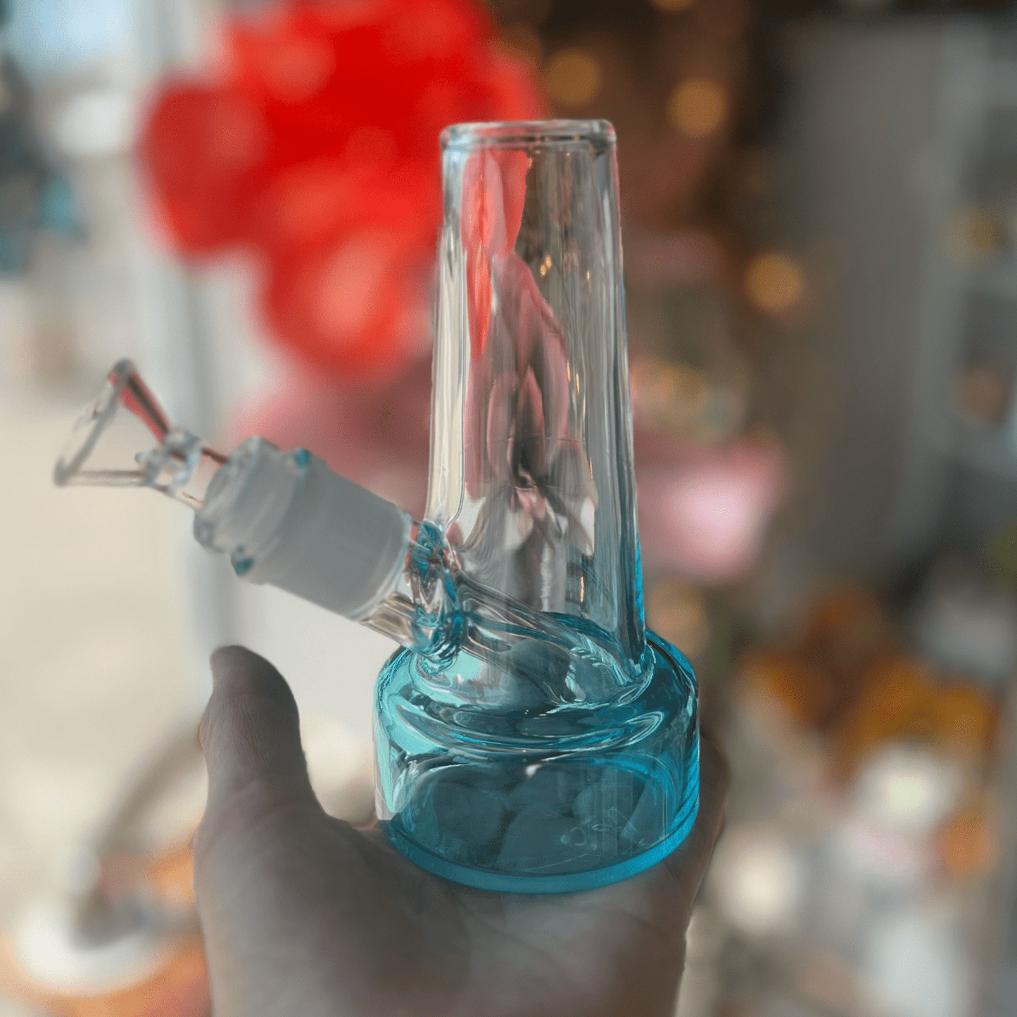 A close-up, angled view of the Ombré Bubbler, featuring a clear glass piece held against a blurred, colorful backdrop.