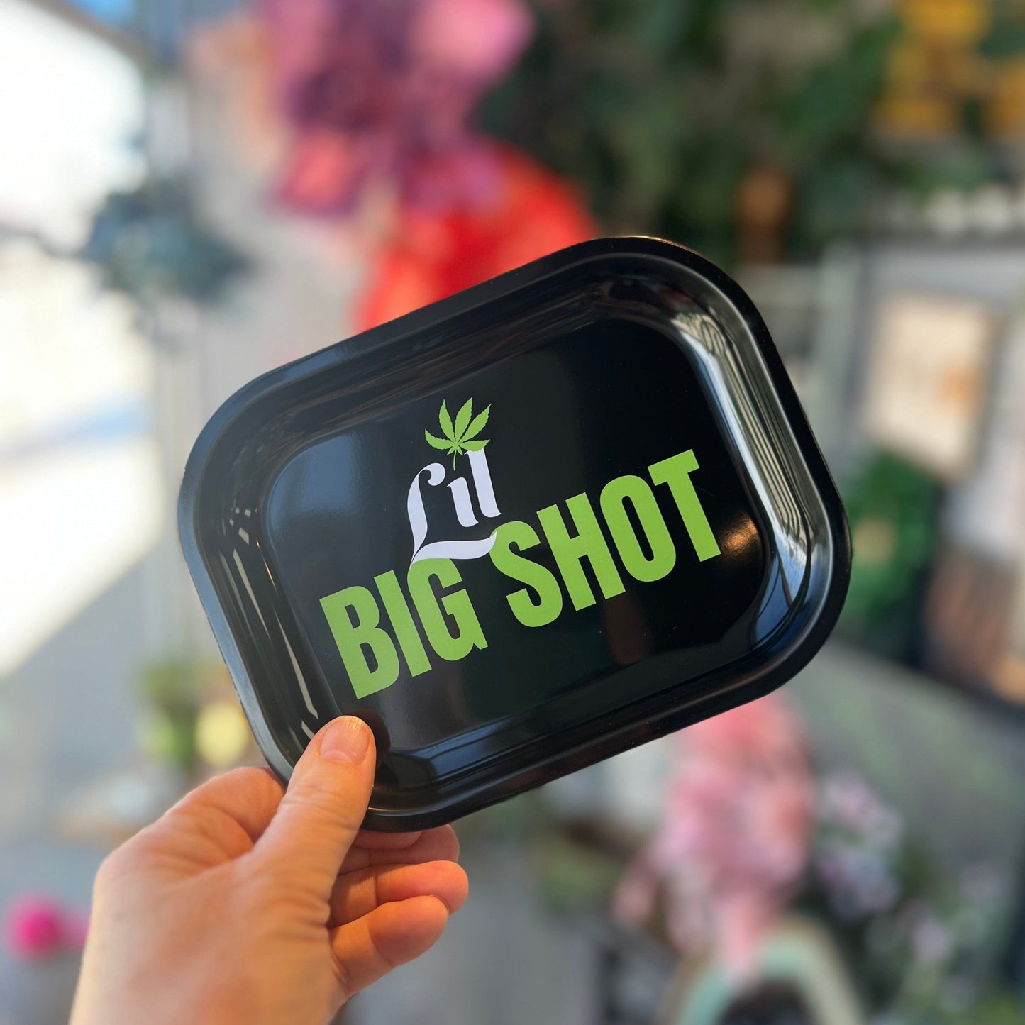 A hand holds the Lil Big Shot Bubbler against a blurred floral background, showcasing its compact size and smooth design.