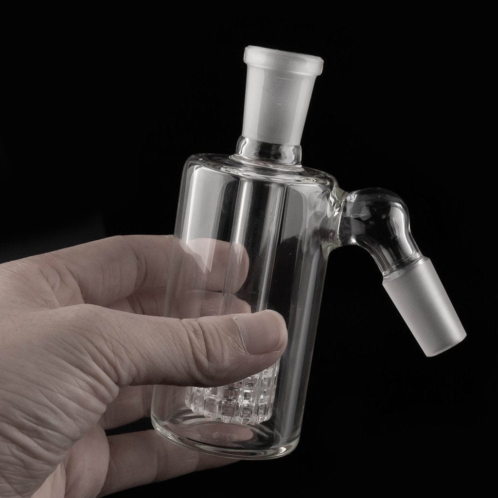 A hand holds the Matrix Ash Catcher, showcasing its clear glass construction and unique, multi-faceted design.
