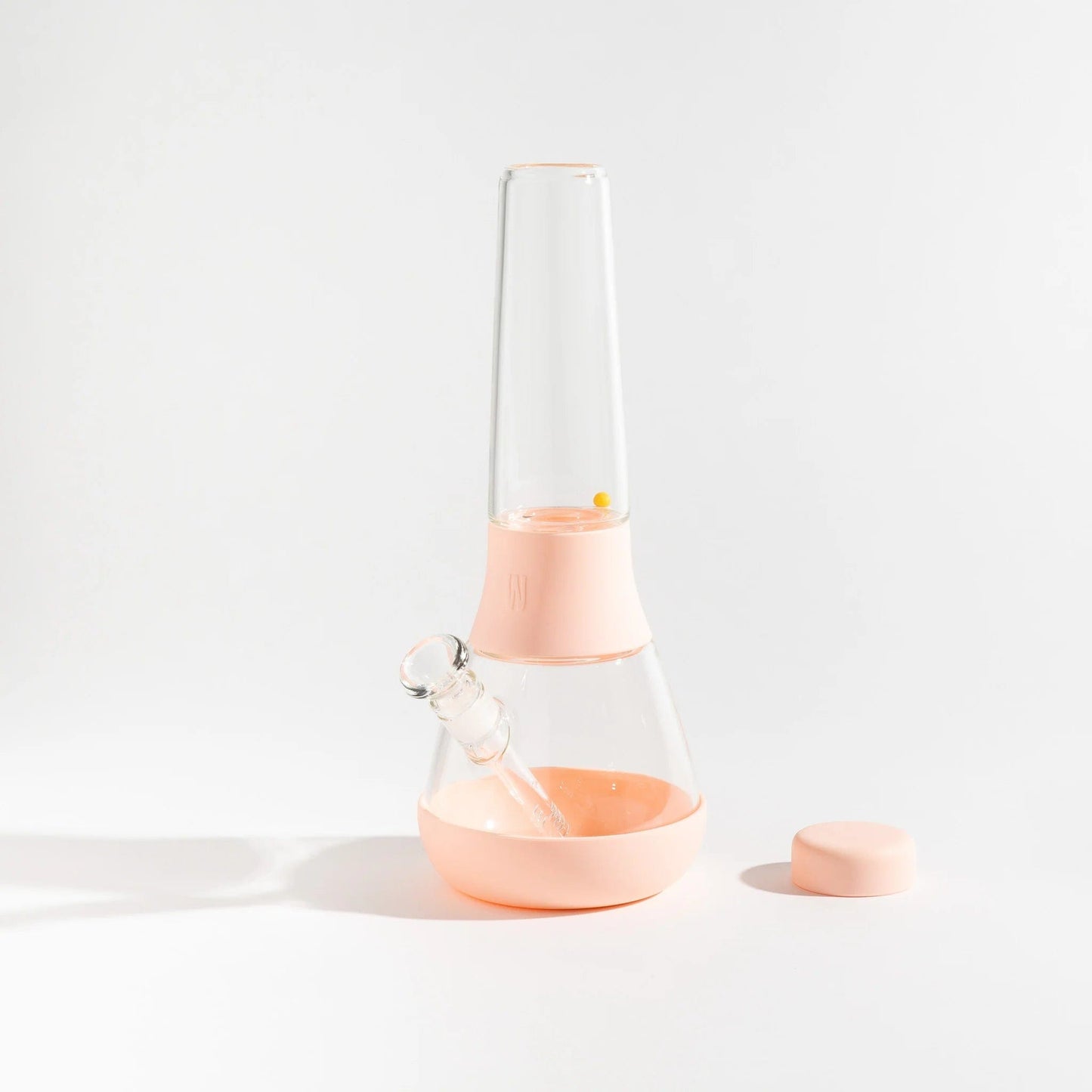 A front view of The Bong By Weeday, a clear glass piece with a rounded base and simple design, sits on a light surface.