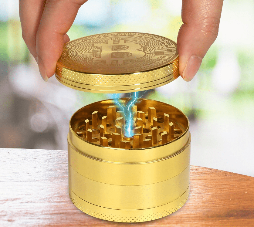 A close-up, angled view of the 4 Piece Small Bitcoin Metal Grinder, with its lid partially open on a light wooden surface.