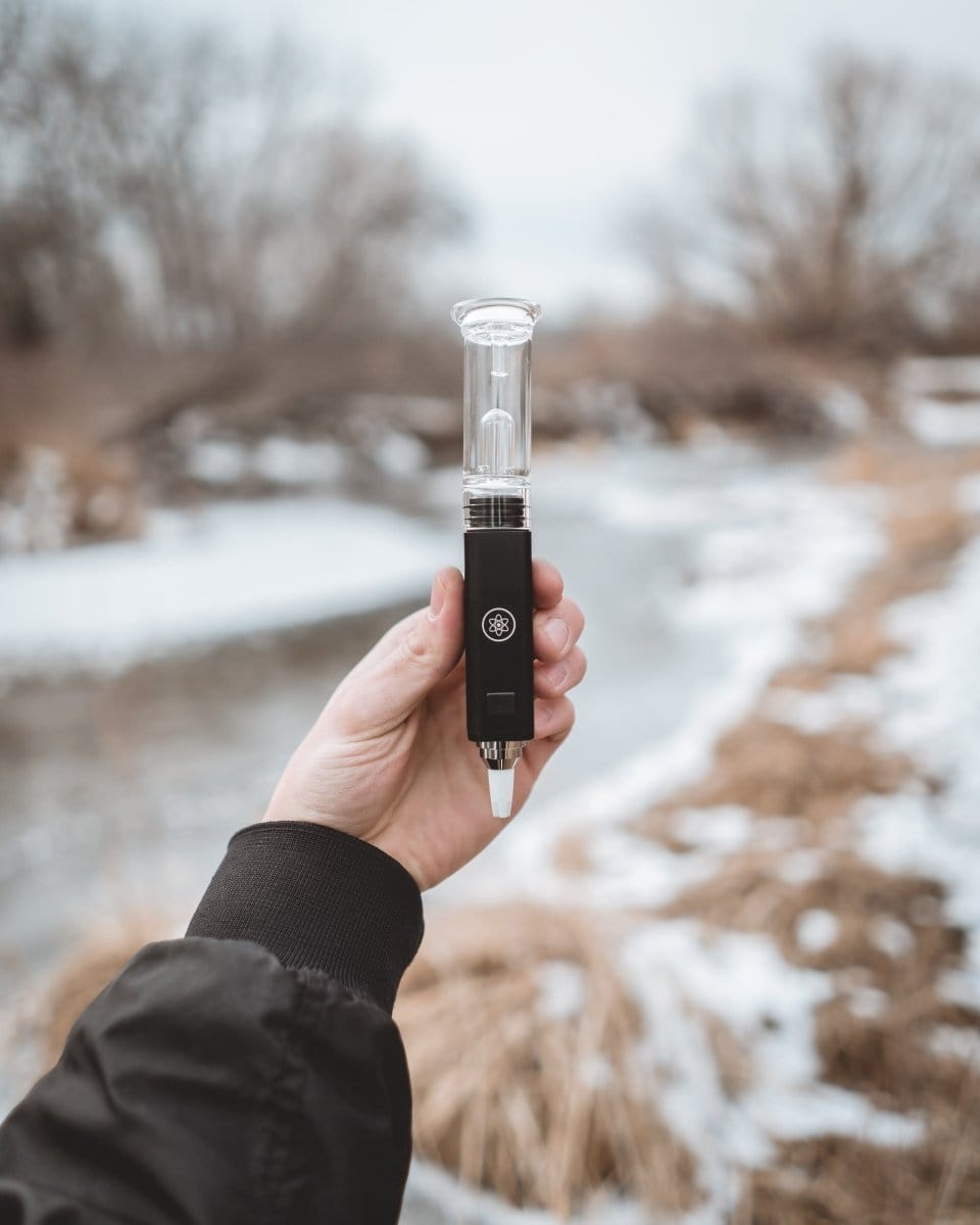 A hand holds the DabTech Daborizer against a blurred, wintry background, showcasing its sleek, pen-like design.