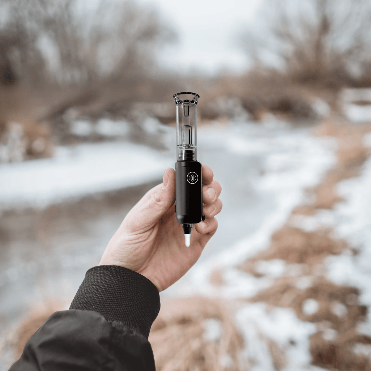 A hand holds the DabTech Trio, highlighting its sleek design against a blurred, neutral background.