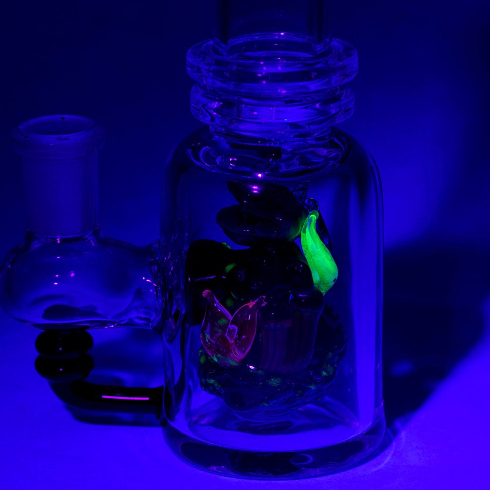 A slightly angled view of the “Save the Seas” Mini Tube, featuring clear glass and a subtle blue tint against a dark blue background.