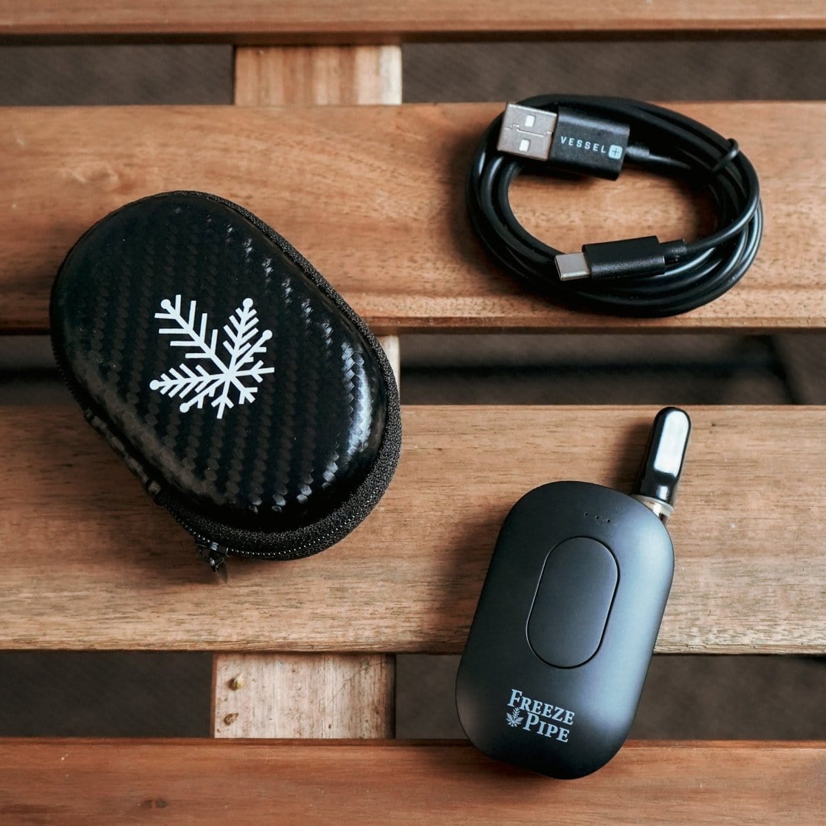 Close-up of the Freeze Pipe Vape Pen and its charging cable on a dark surface.