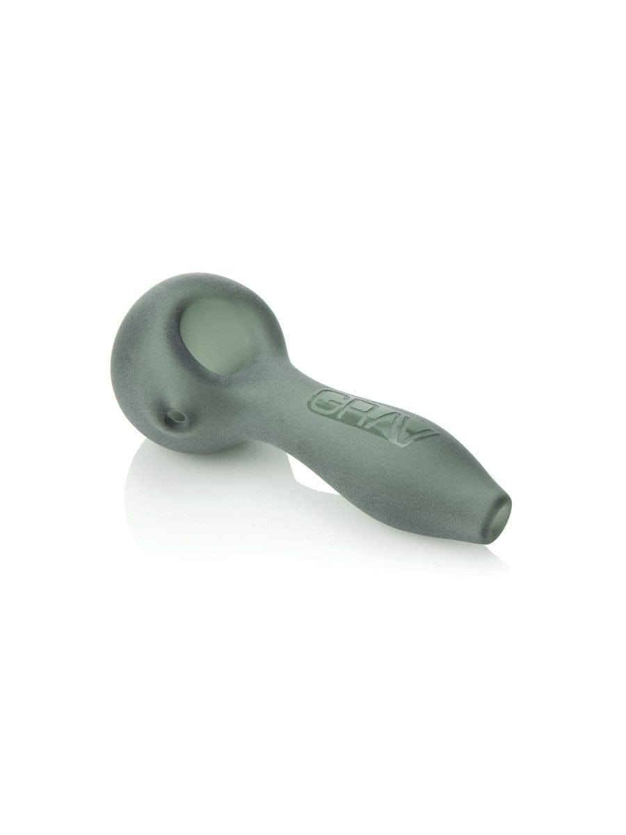 A three-quarter view of the GRAVĀ® Sandblasted Spoon Pipe, resting on a reflective surface with soft, diffused lighting.