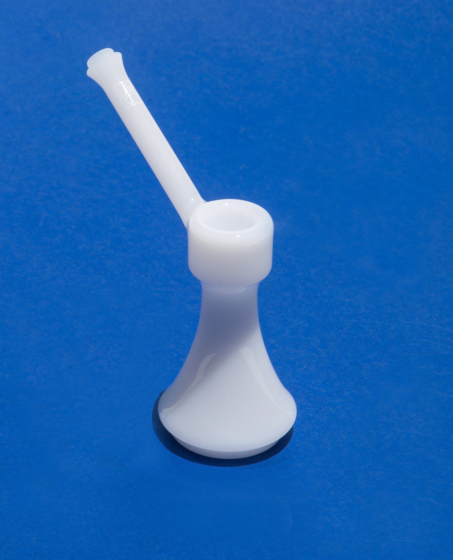 Front view of The Bubbler By Jane West, a clear glass bubbler with a simple, rounded form against a solid blue background.