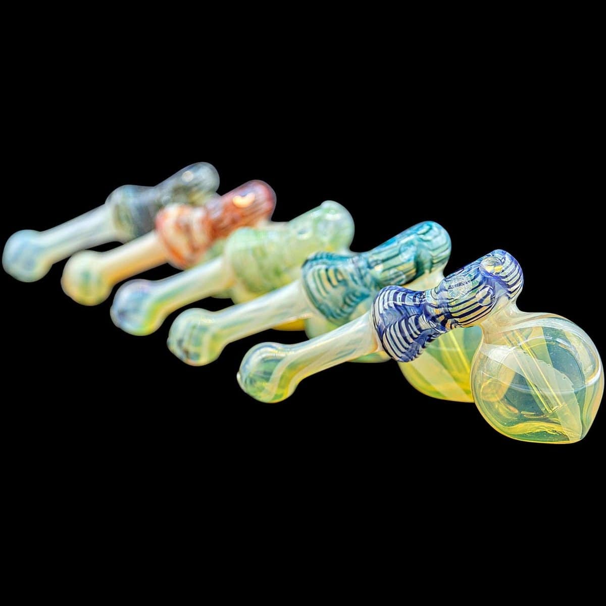 A side view of several “Raked Hammer” Fumed Hammer Bubbler Pipes in various colors, arranged on a black background.