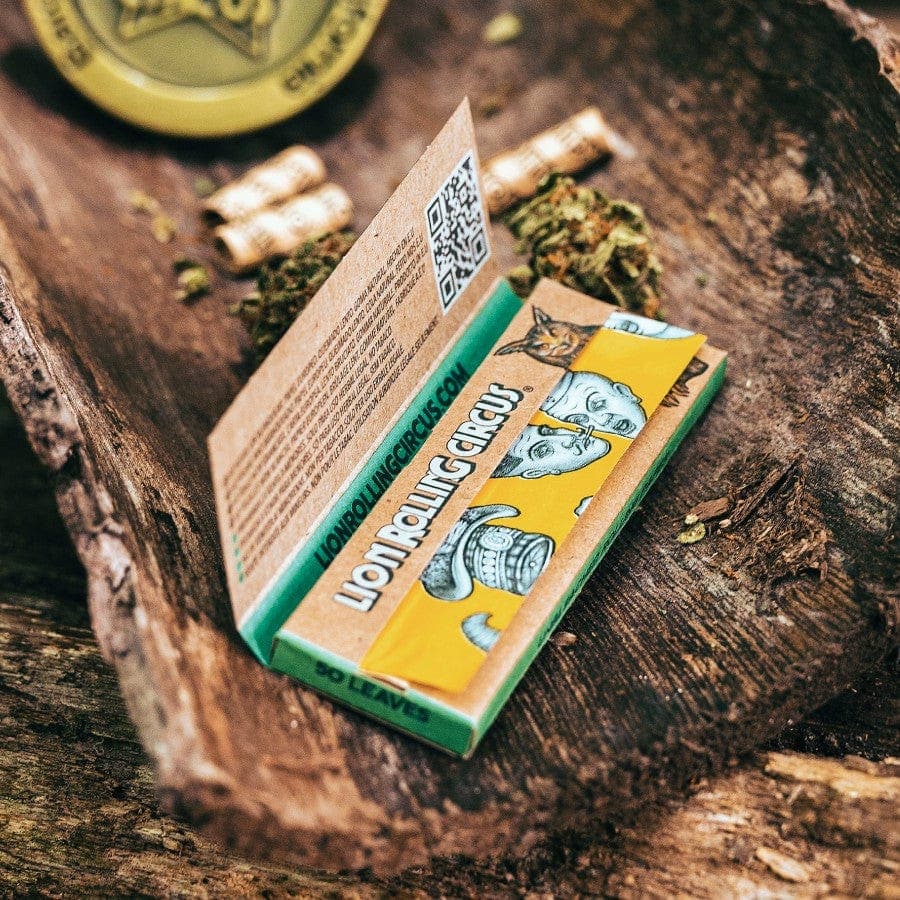 A close-up, angled view of Lion Rolling Circus Unbleached 1-1/4 Rolling Papers packaging on a textured wooden surface.