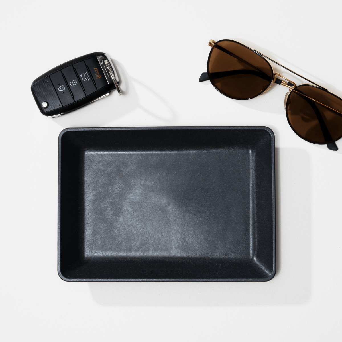 Overhead view of the Eco-Tray, a minimalist rectangular tray, shown with sunglasses beside it on a light surface.