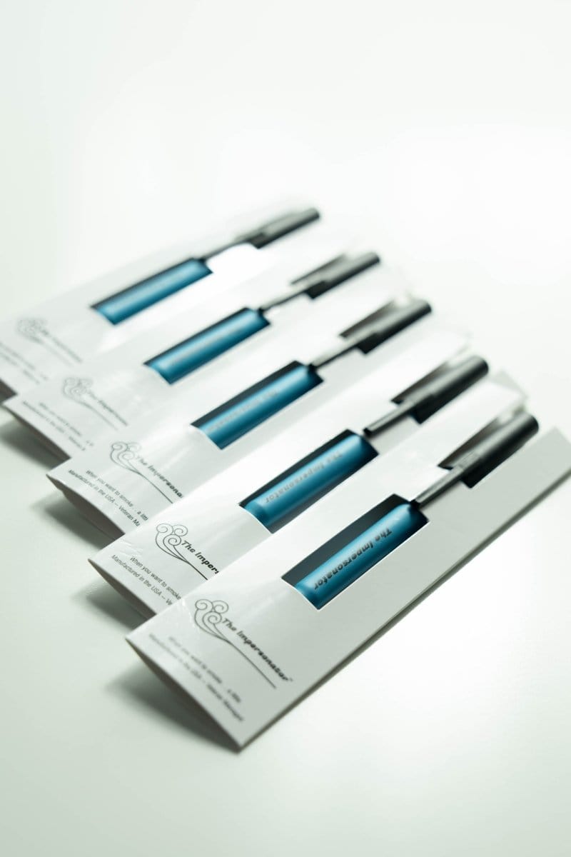 A low-angle view showcases The Impersonator 5-Pack, a collection of clear glass tubes arranged diagonally on a white surface.