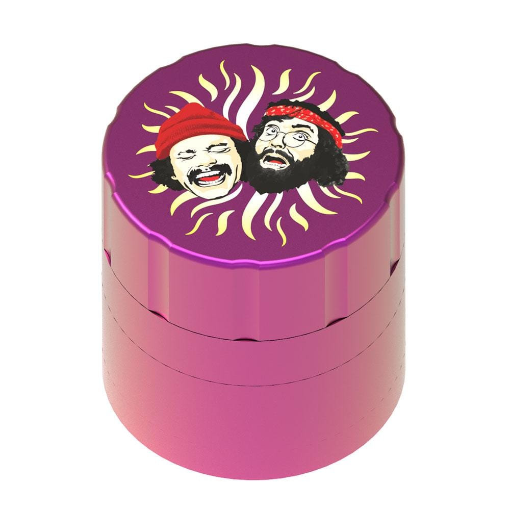 Top-down view of a purple Up In Smoke 40th Anniversary 53mm 4-Piece Grinder showing a sunburst graphic with two laughing faces on the lid.