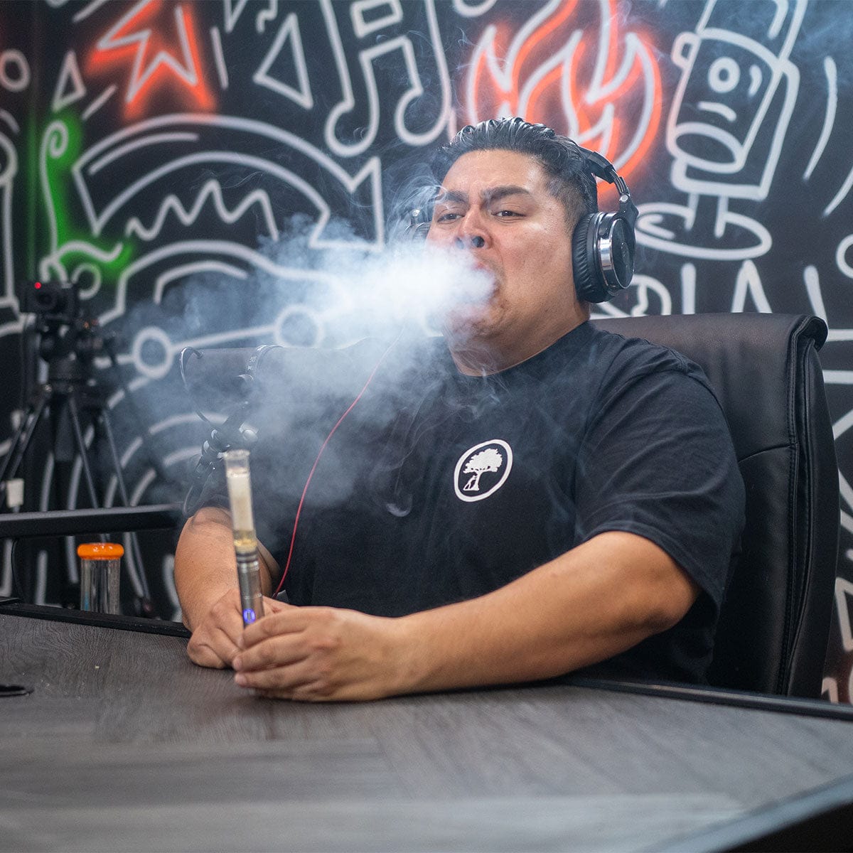 Three-quarter view of a man exhaling a large cloud of vapor while seated with the Cipher NOVA | Stainless Steel - V2 held in his hands.