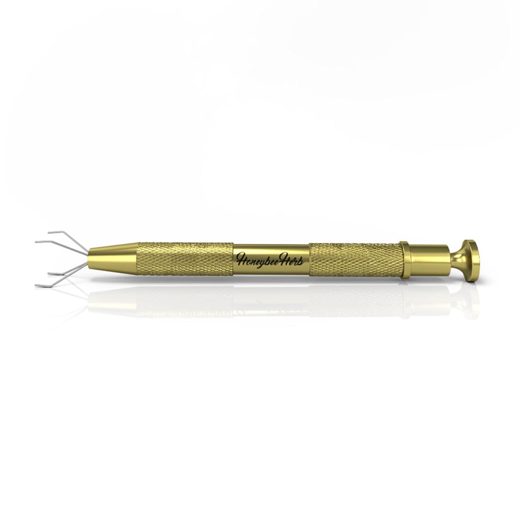 Close-up side view of the gold Honeybee Herb Dab Claw with textured grip, extended metal prongs, and reflective white background