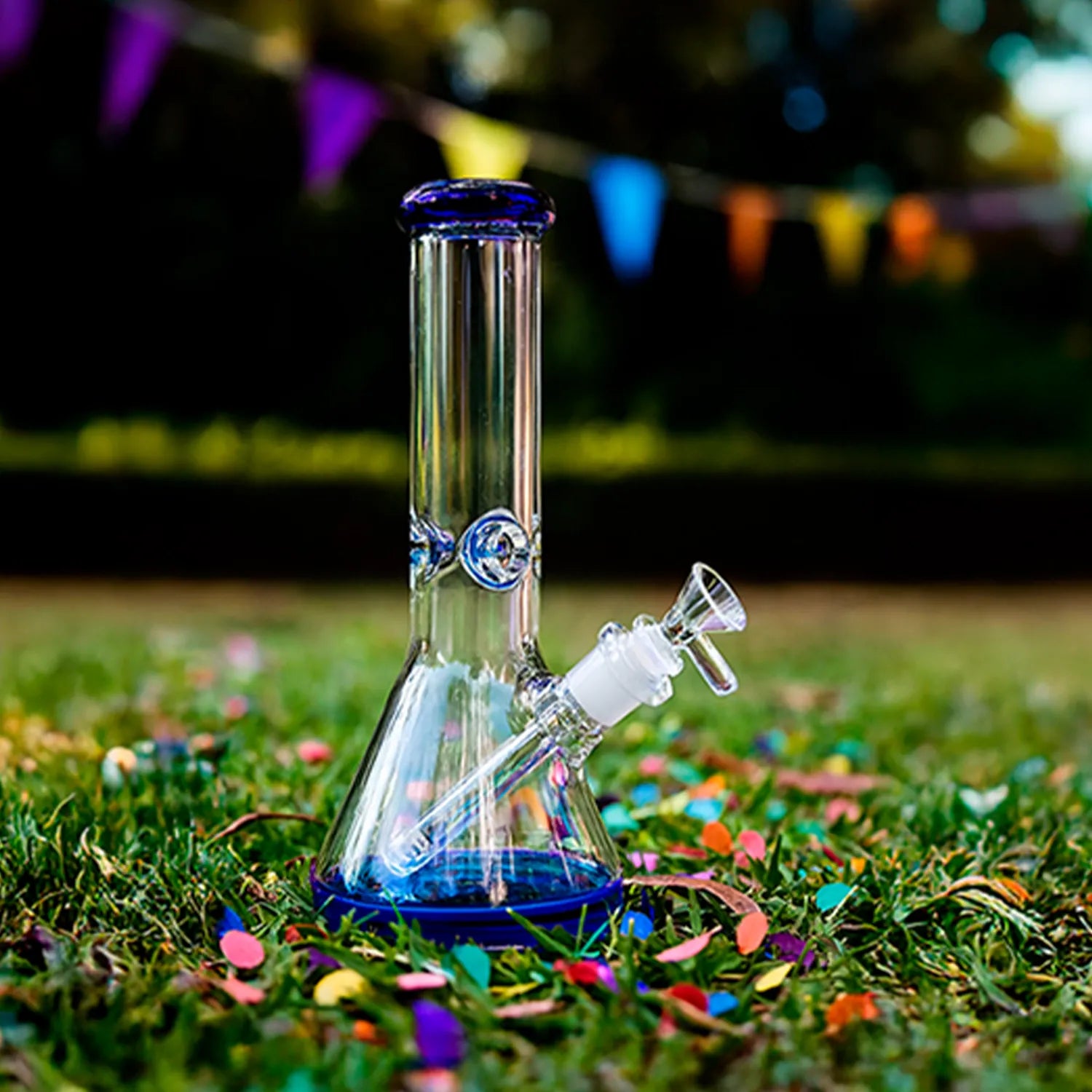 Close-up, low-angle view of the DHC 9mm Big Base Beaker w/ Color Accents Bong - 12 in. standing on grass with blue accents.