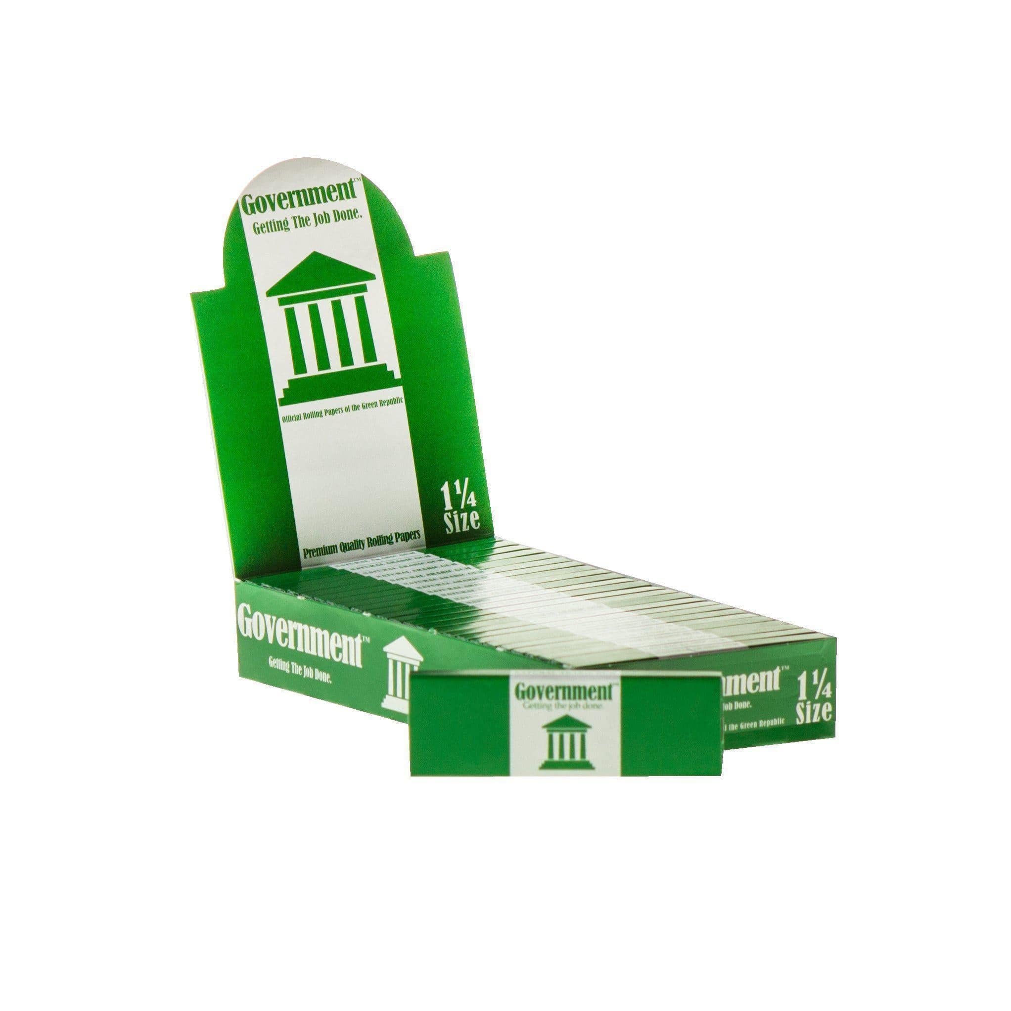 Angled close-up of a green countertop display of Government Rolling Papers - King Size showing stacked packs and a white column logo.