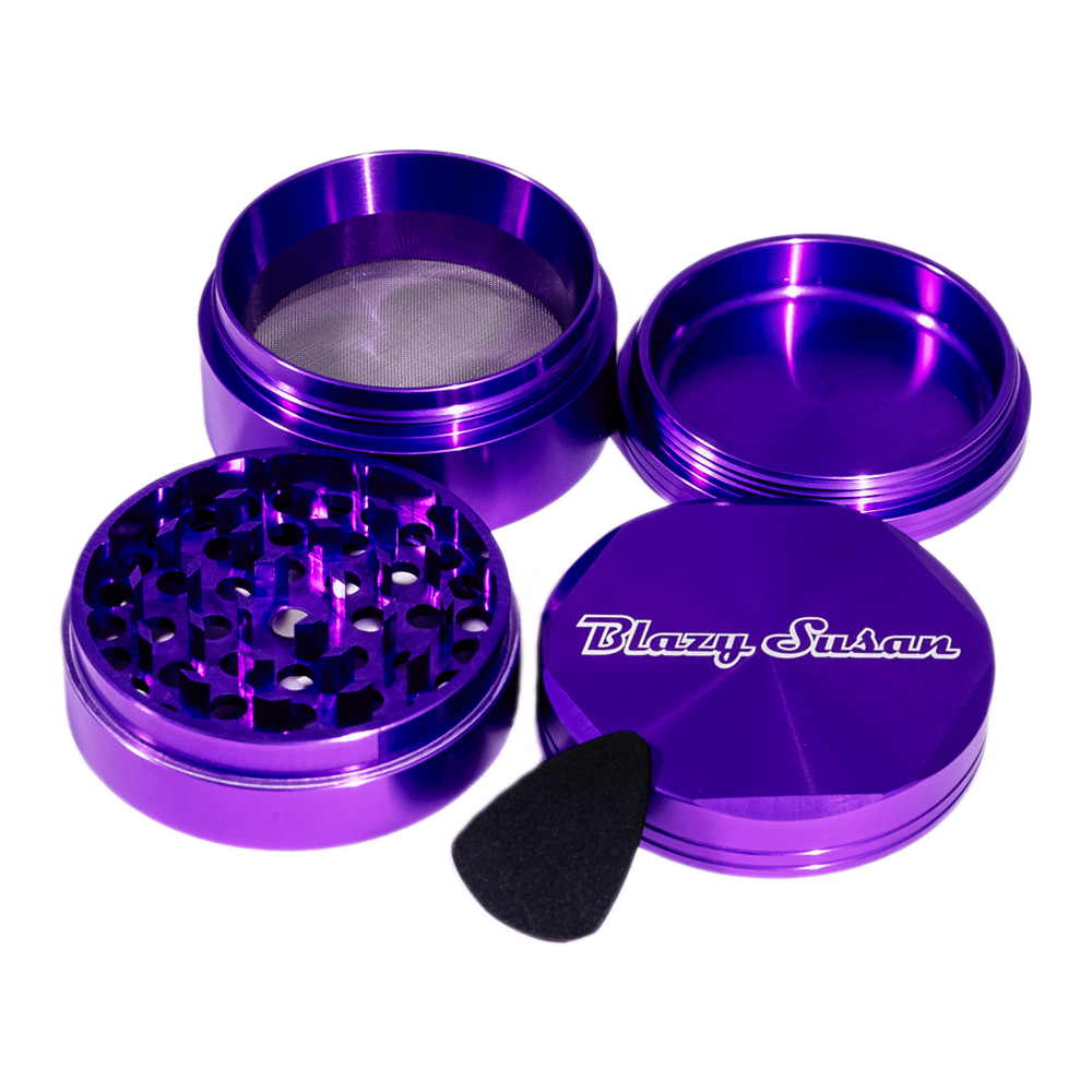 Top-down view of the purple Blazy Susan 4-pc 3 Chamber Grinder with its stacked open chambers, lid showing brand logo, and scraper.