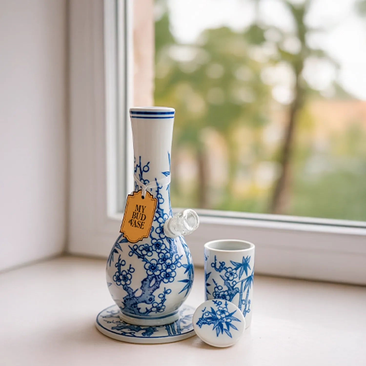 Close-up of the My Bud Vase "Luck" Chinese Porcelain Vase Bong on a windowsill, shown from a slight front-left angle with blue floral patterns and soft daylight.
