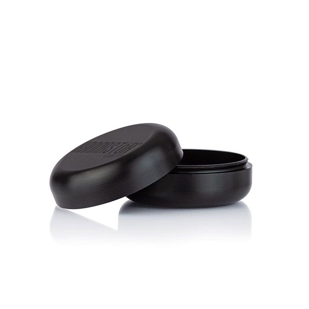 Angled close-up of the black Ryot Gr8Tr Solid Body Grinder with its lid propped beside the open base on a white reflective surface