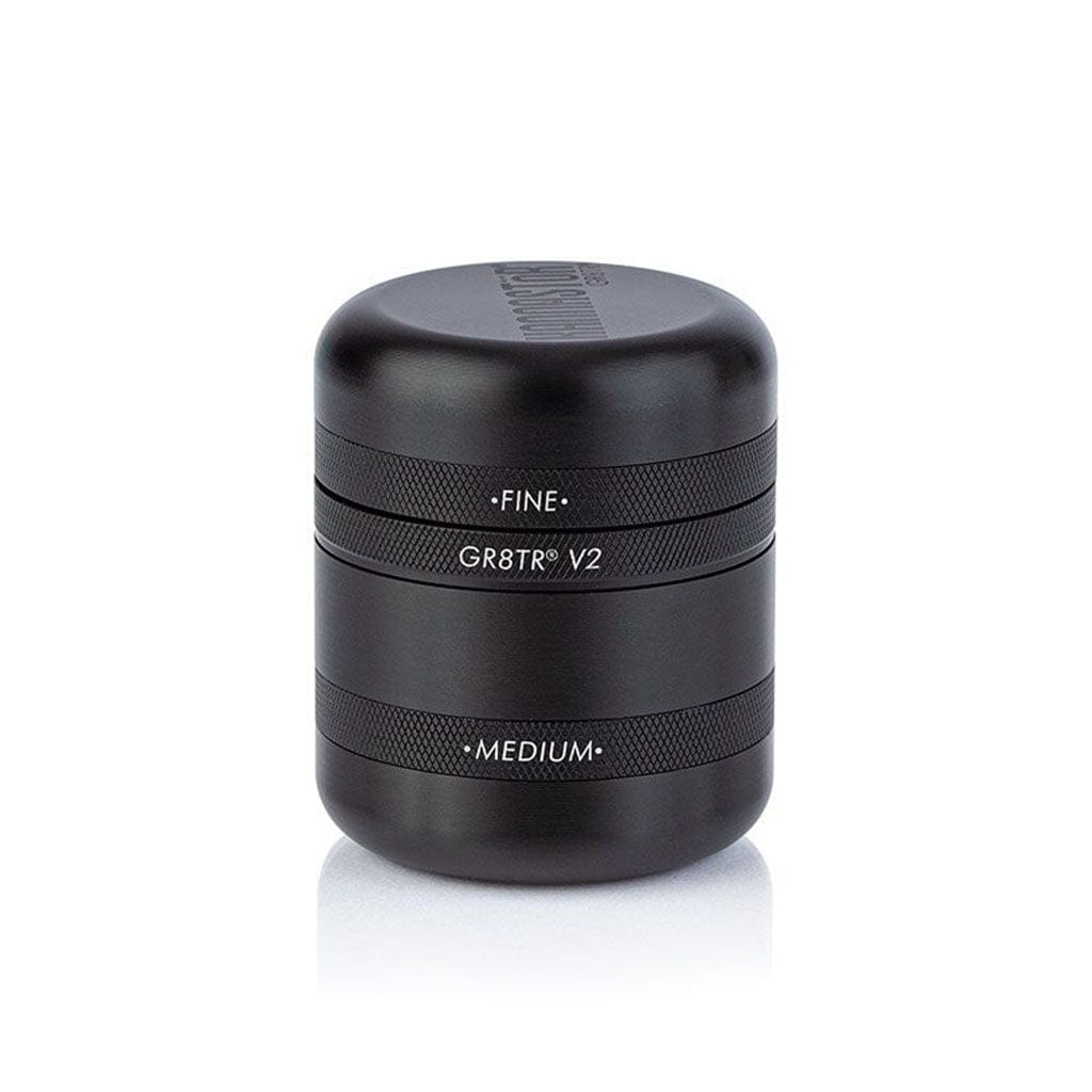 Front three-quarter view of a matte black Ryot Gr8Tr Solid Body Grinder sitting on a white reflective surface, showing stacked textured rings labeled "FINE," "GR8TR V2," and "MEDIUM."