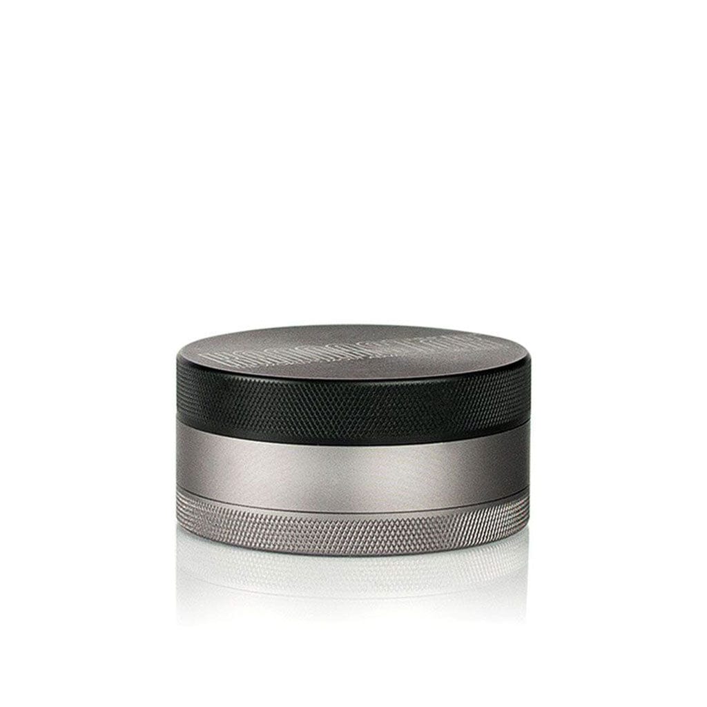 Centered front view of a two-tone metal Ryot 4Pc Jar Body Grinders resting on a white reflective surface, showing textured lid and base.