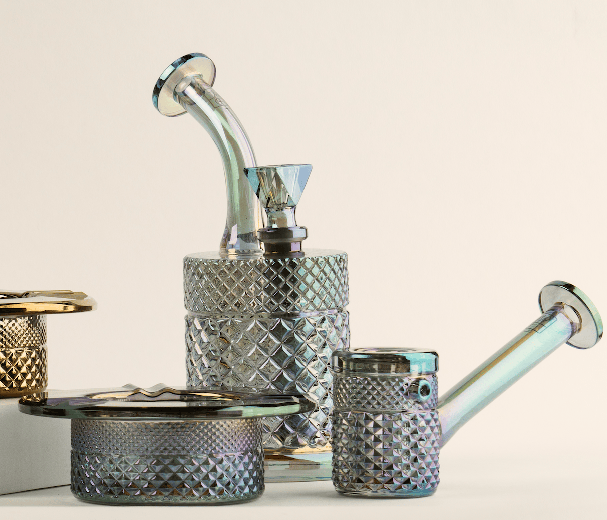 Angled front view of the iridescent Twenties Collection Hand Pipe | Mermaid showing its textured diamond-cut glass body, bent neck, and matching ashtray on a pale background