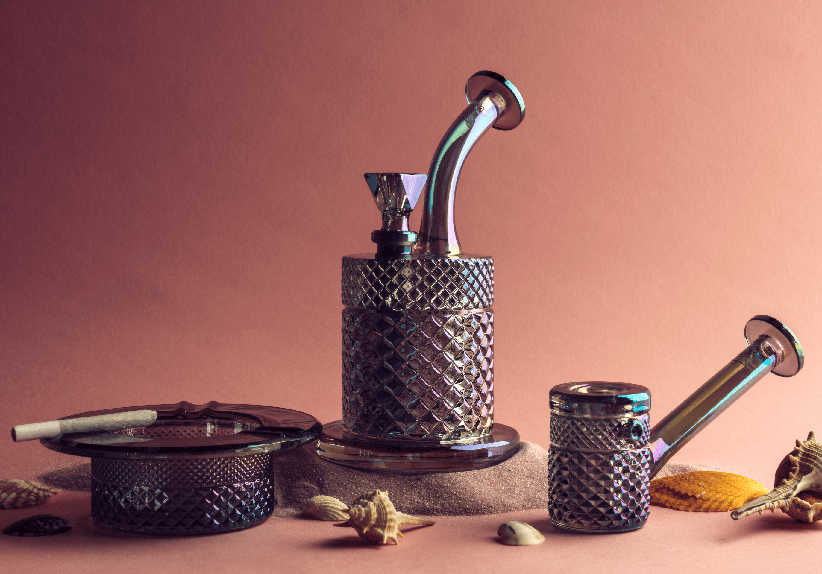 Close-up, angled view of the Twenties Collection Hand Pipe | Mermaid showing iridescent glass textures atop a diamond-patterned base against a soft pink backdrop