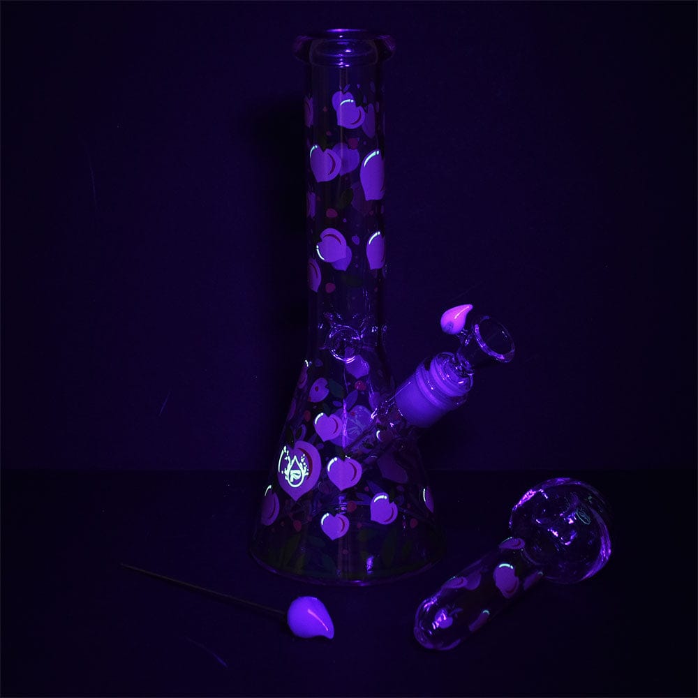 Front three-quarter view of the Pulsar Fruit Series Peaches & Cream Herb Pipe Glow Duo - 10" / 14Mm F standing on a dark surface with glowing peach motifs under purple blacklight.