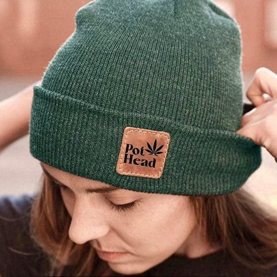 A close-up, angled view shows the dark green Pot Head Beanie worn by a person, with subtle lighting highlighting the knitted texture.