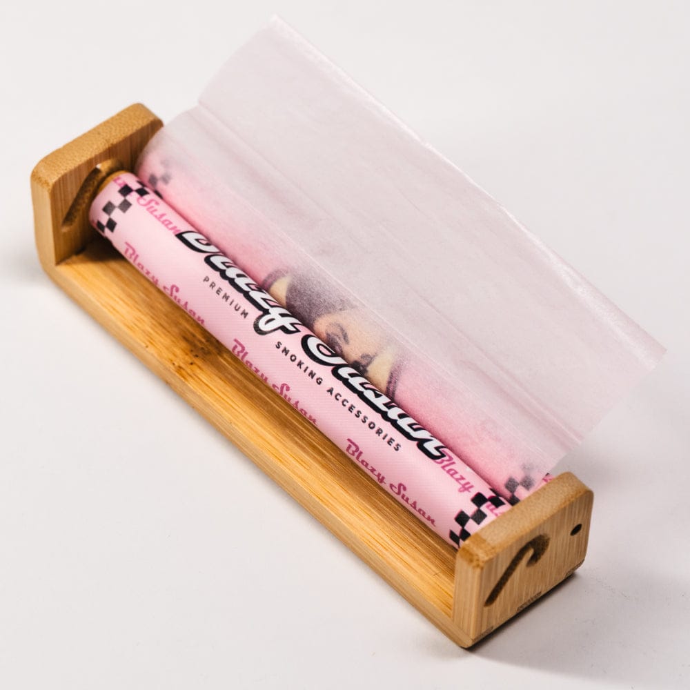 Angled close-up of a bamboo roller holding a pink Blazy Susan Accessories, Bamboo Roller, King Size Regular 110mm, Display Box paper roll with a sheet partially unrolled.