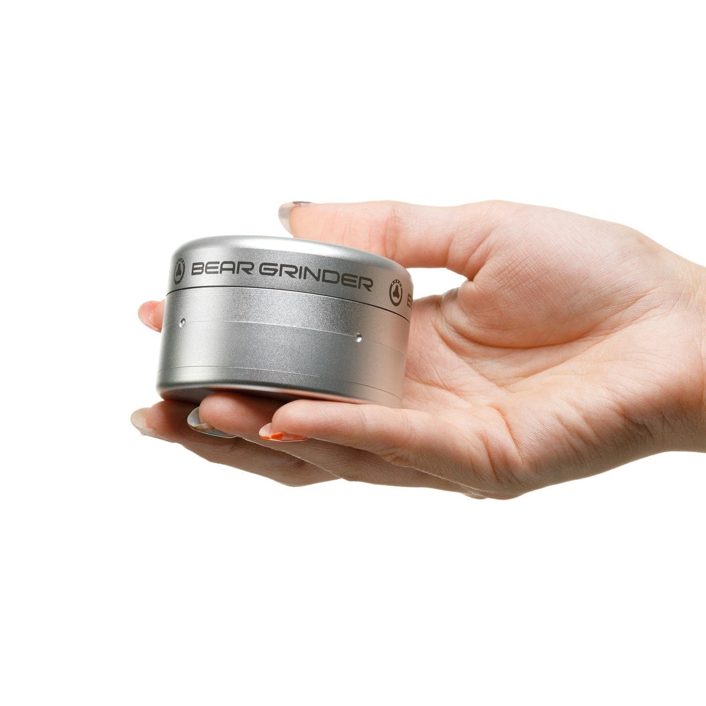 A hand holds the 4 Piece Grinder, showcasing its circular shape and metallic finish in a bright, neutral setting.