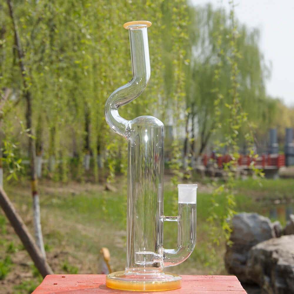 A front view of the NATTY BONG, a clear glass piece resting on a red surface with a blurred green background.