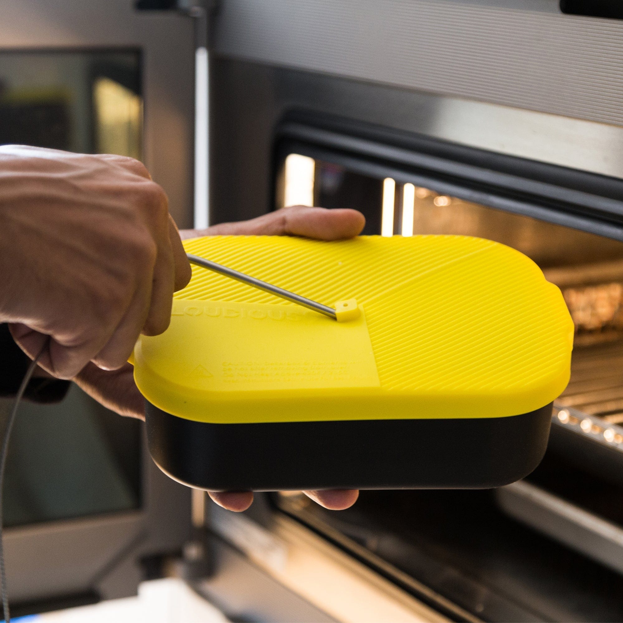 A hand holds the Decarb9 Herbal Decarboxylator Kit, its rectangular form positioned against a blurred, metallic interior.