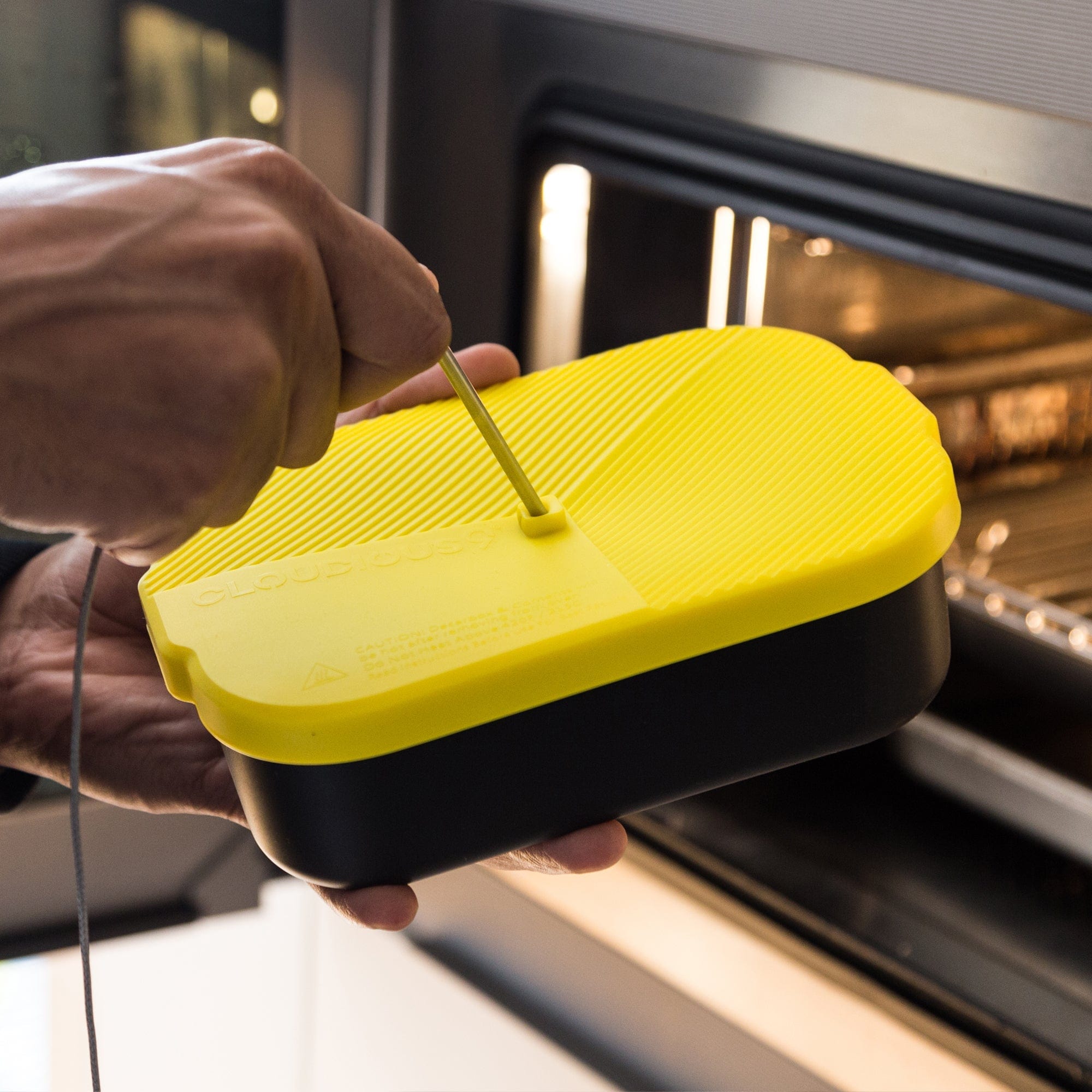 A close-up, angled view shows the Decarb9 Herbal Decarboxylator Kit’s black container with a textured, yellow lid being held by a hand.