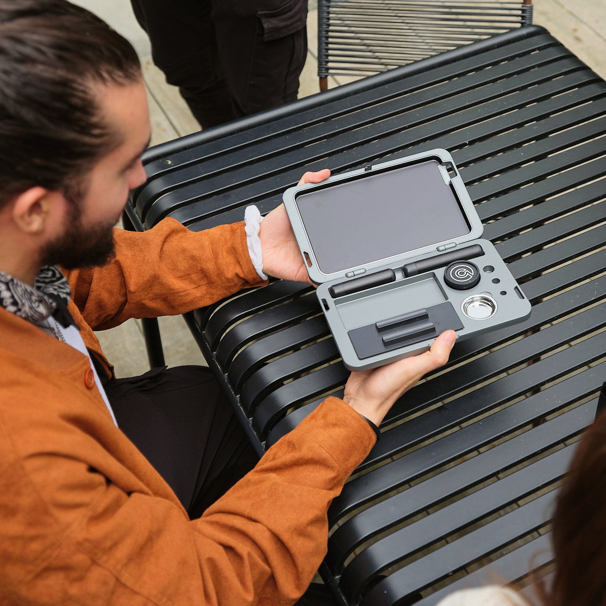 A close-up, angled view shows a person holding the M.L.T.9 Portable Rolling Tray Survival Kit against a dark, ribbed background.