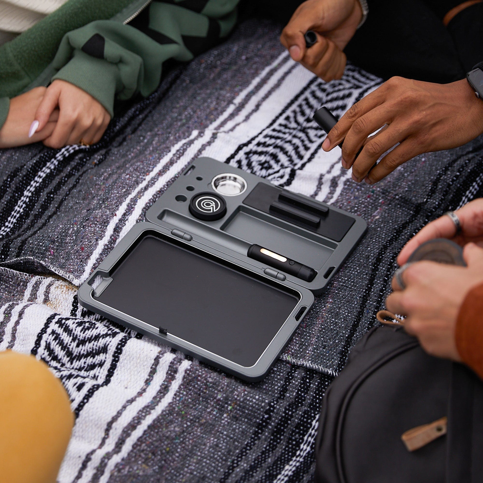 Overhead view of the M.L.T.9 Portable Rolling Tray Survival Kit resting on a patterned blanket next to a person's hands.