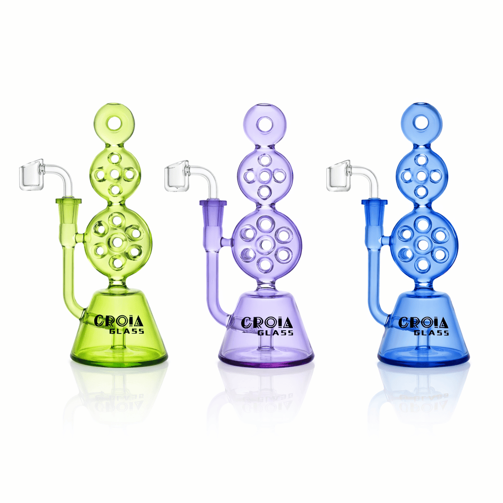 Front view of three colored Croia Glass 8" Triple Stack Swiss Perc Recycler Dab Rig | Croia Glass pieces—green, purple, and blue—on a white reflective background.
