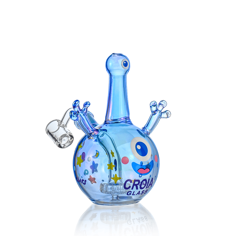 Three-quarter front view of the Croia Glass Cyclops Monster Mini Dab Rig with Showerhead Perc | Croia Glass, a small iridescent blue cyclops-shaped rig with a round body, raised arm-like percs, colorful star stickers and reflection on a white background