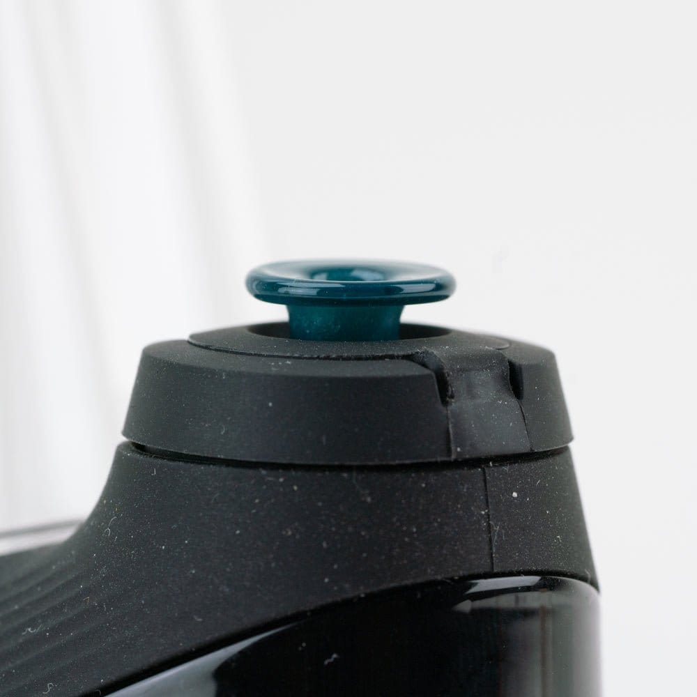 Close-up front view of the Empire Glassworks PuffCo 'New Peak' & Proxy Glass Joystick Cap - Blue Lagoon showing the teal-blue glass joystick cap seated in a black device top against a soft white background