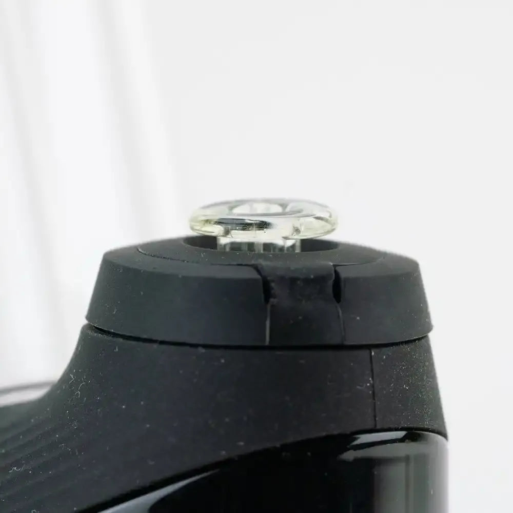 Close-up side view of the Empire Glassworks PuffCo 'New Peak' & Proxy Glass Joystick Cap - Eclipse showing a clear glass joystick button mounted on a matte black circular rubber cap against a soft white background.