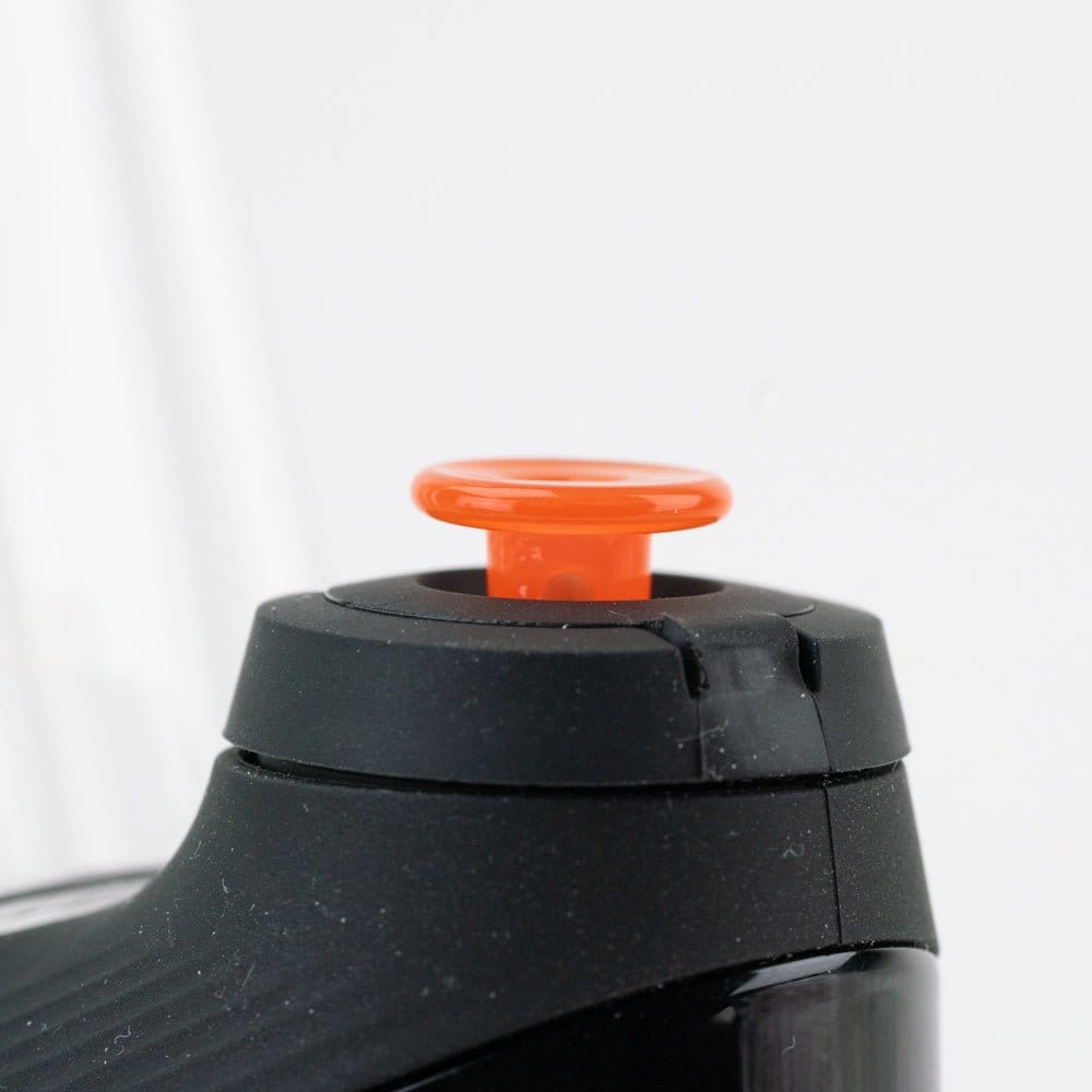 Close-up, slightly elevated view of the Empire Glassworks PuffCo 'New Peak' & Proxy Glass Joystick Cap - Orange mounted on a black device, showing its glossy orange mushroom top and matte black housing.