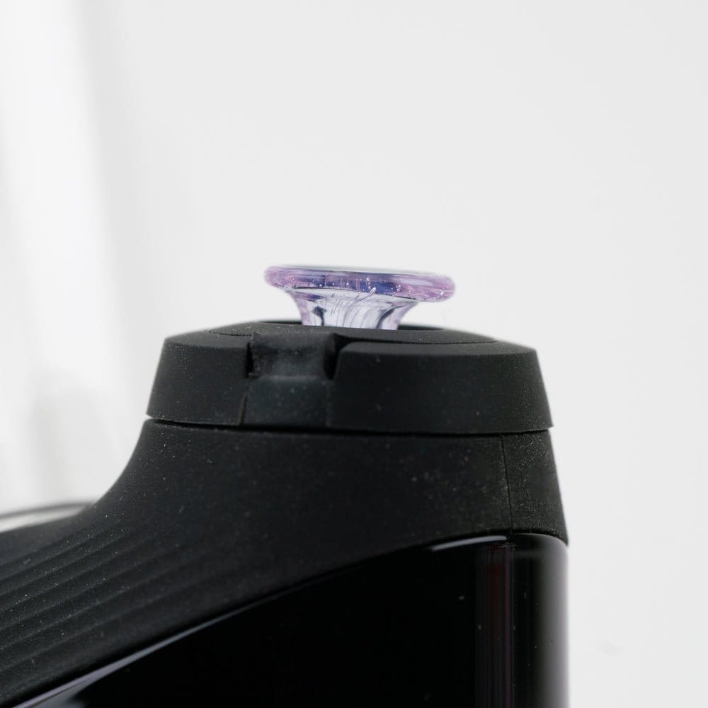 Close-up side view of the Empire Glassworks PuffCo 'New Peak' & Proxy Glass Joystick Cap - Pink Slyme fitted atop a black device, showing the translucent purple-pink glass cap against a soft white background.