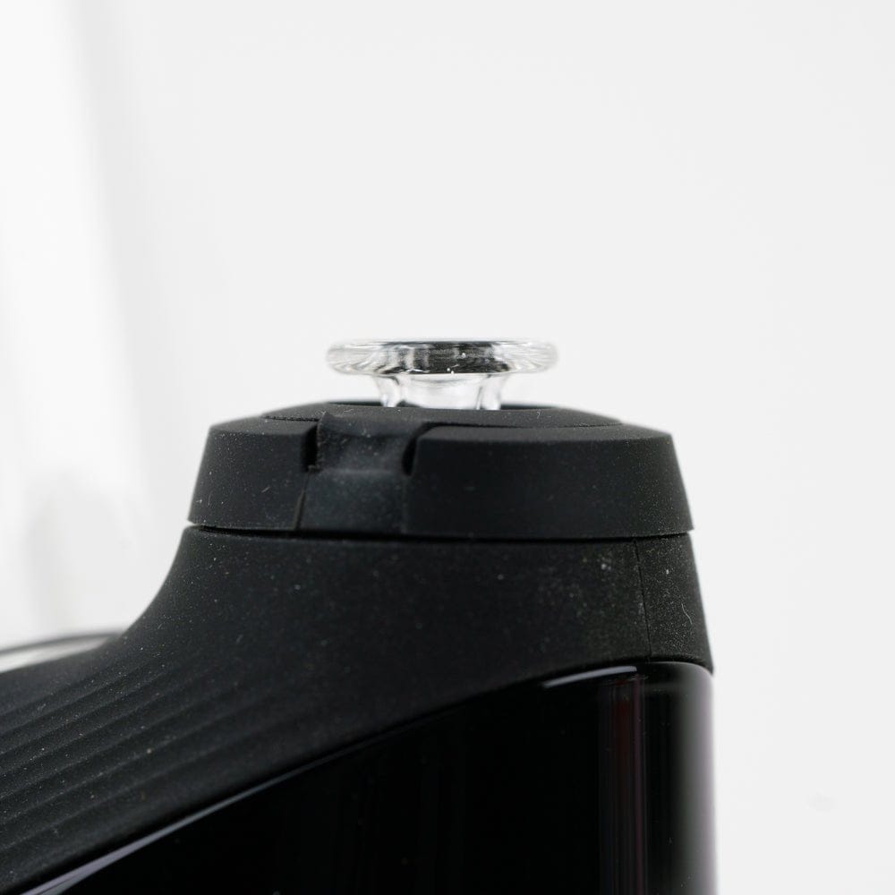Close-up, slightly low-angle view of the Empire Glassworks PuffCo 'New Peak' & Proxy Glass Joystick Cap - Pink UV mounted on a black device, showing the clear glass joystick against a soft white background.