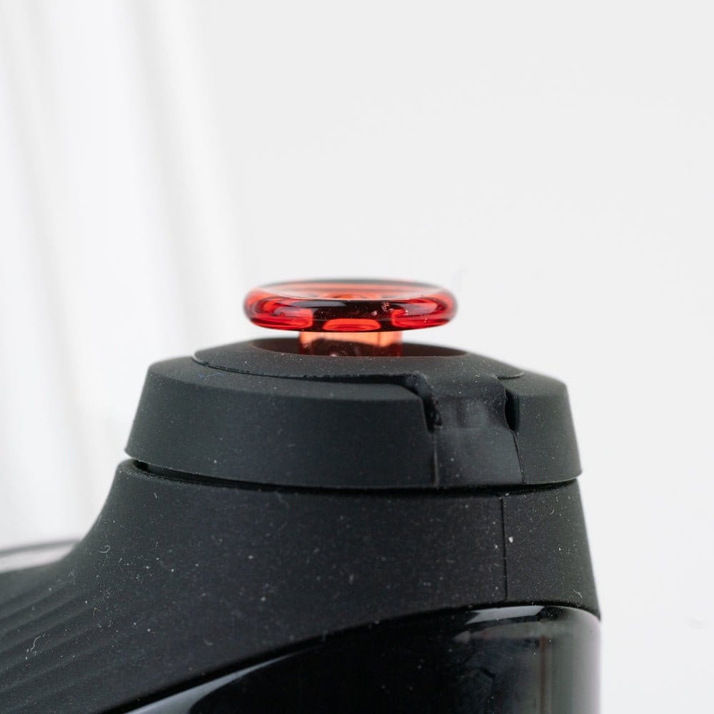 Close-up, slightly low-angle view of the Empire Glassworks PuffCo 'New Peak' & Proxy Glass Joystick Cap - Translucent Red seated on a black device, showing the glossy red translucent cap against a soft white background.