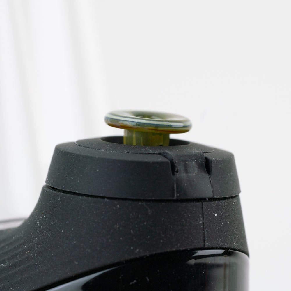 Close-up of an Empire Glassworks PuffCo 'New Peak' & Proxy Glass Joystick Cap showing the green-tinted glass cap seated on a black device top against a soft white background