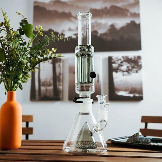 A front view of the Freeze Pipe XL Bong, displaying its clear glass construction alongside a wooden table and a blurred background.