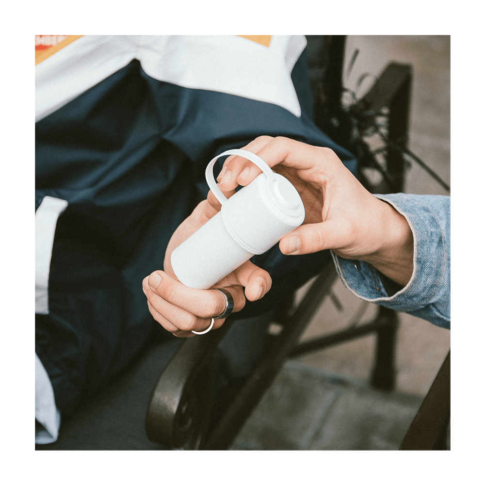 A hand holds The Keeper™ By Hemper, a white container with a minimalist design, against a dark blue background.
